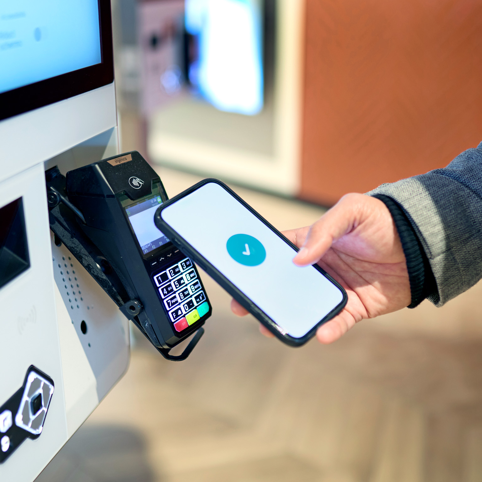A person holds a smartphone near a payment terminal, with a checkmark displayed on the screen indicating a successful transaction. 