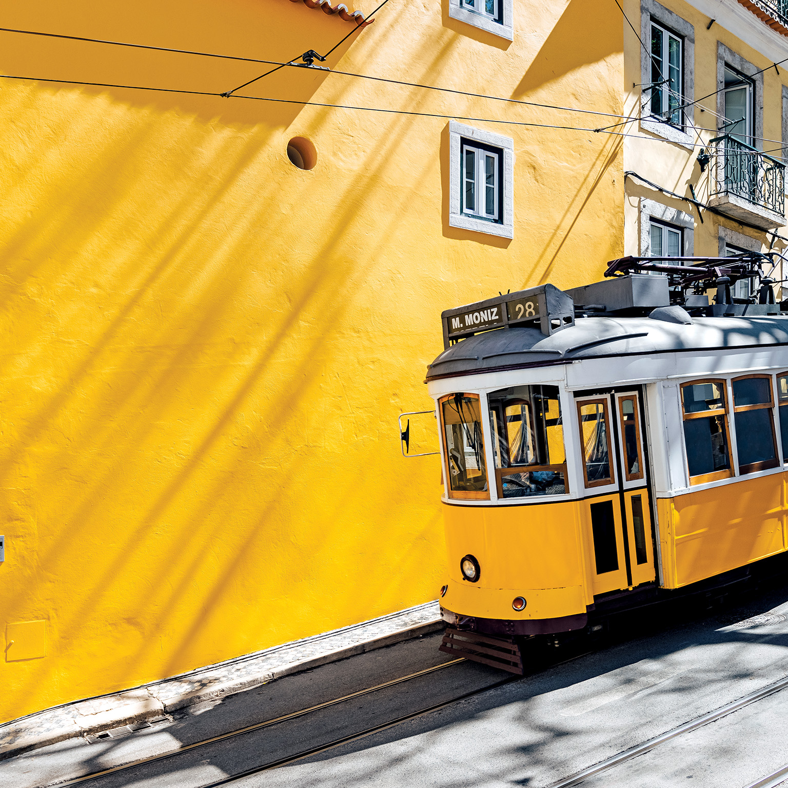 Yellow tram moving past yellow building in Lisbon, Portugal