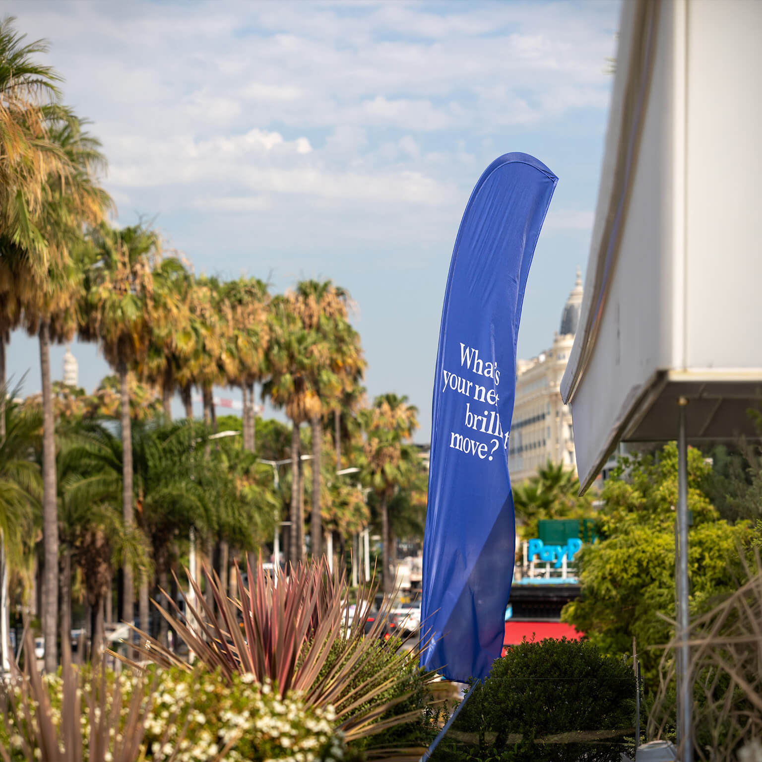 This image was captured during the Cannes Lions International Festival of Creativity. It features a large, blue feather flag prominently displaying the text What's your next brilliant move?