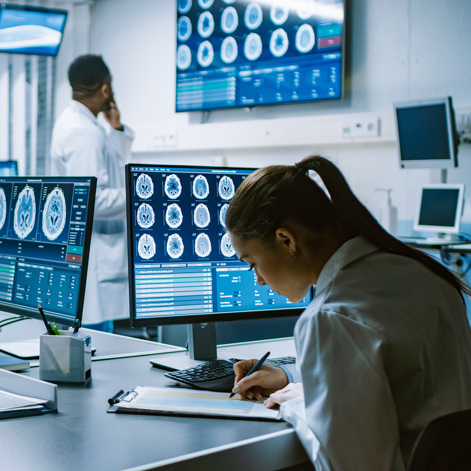 Team of Professional Scientists Work in the Brain Research Laboratory. Neurologists / Neuroscientists Surrounded by Monitors Showing CT, MRI Scans Having Discussions and Working on Personal Computers. - stock photo