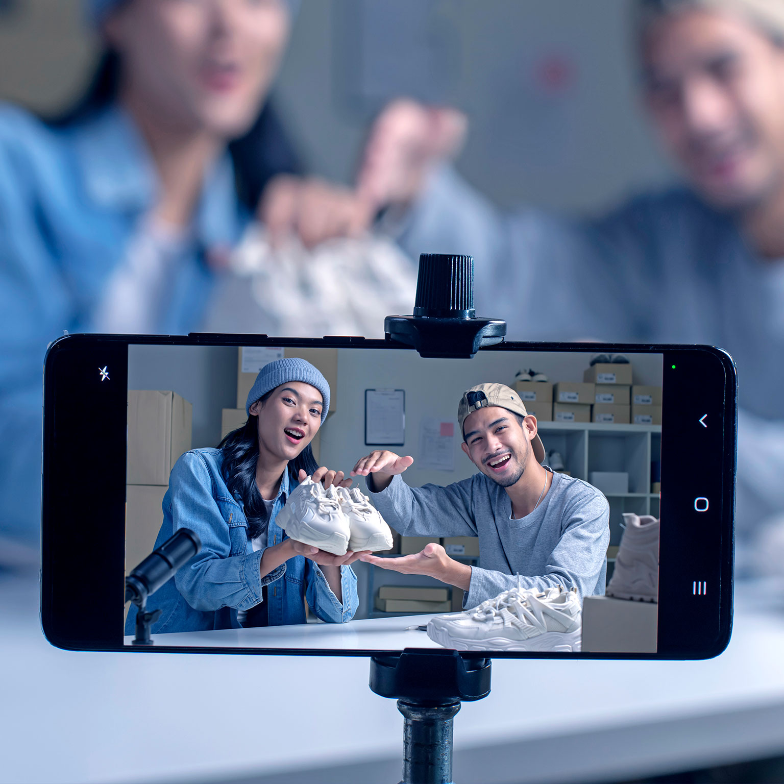 Two people hold up a pair of new sneakers toward a mobile-phone camera, with a microphone in the foreground indicating audio in addition to video recording