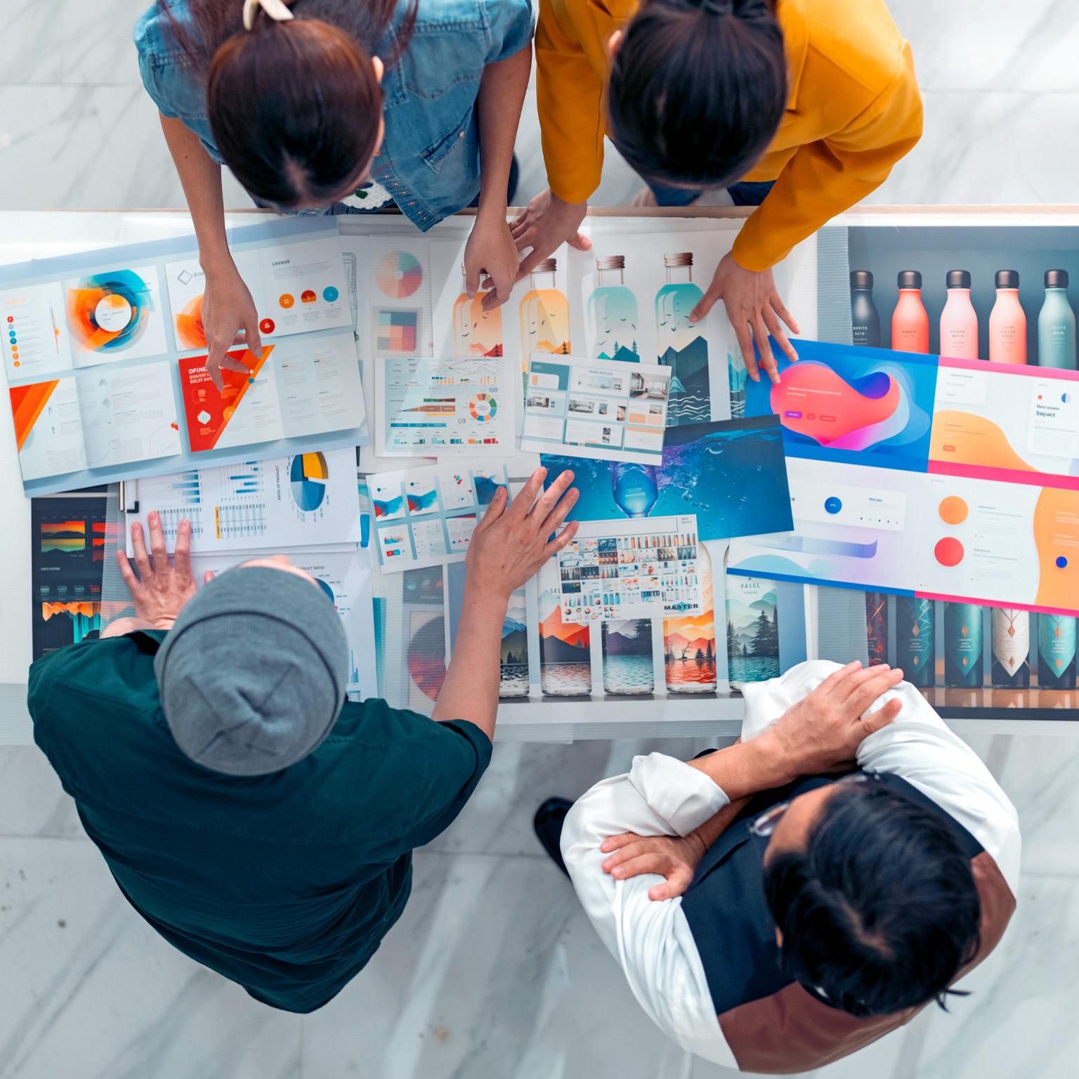 A team of designers gathered around a table, reviewing colorful mockups and data visualizations. The bird's-eye view captures their collaborative effort in a bright and modern workspace.