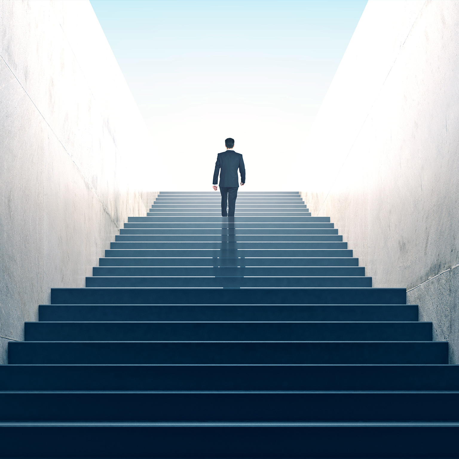 Suited businessperson walking up a multiflight stairway, a few steps from the top