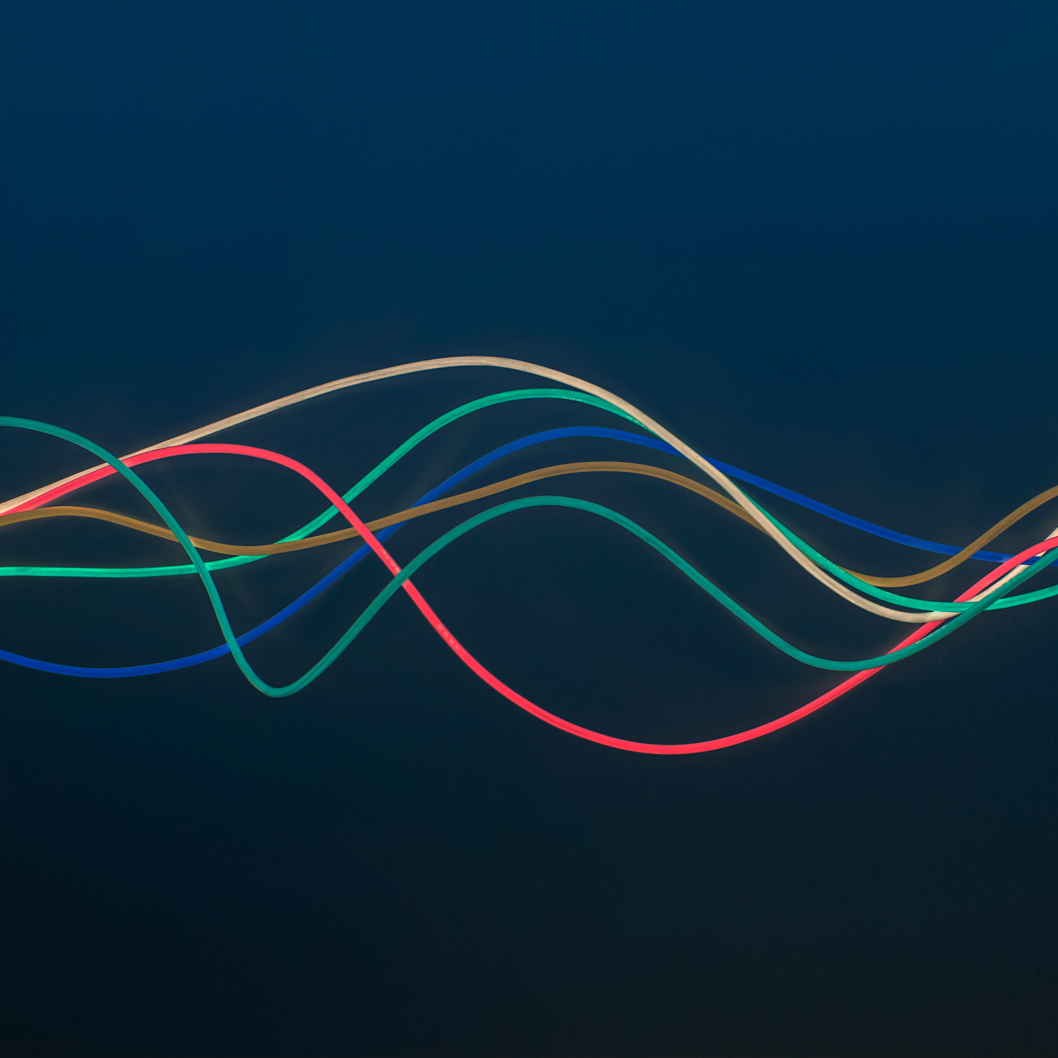 Blue, green, red, brown and white wire in wave pattern on dark blue background - stock photo