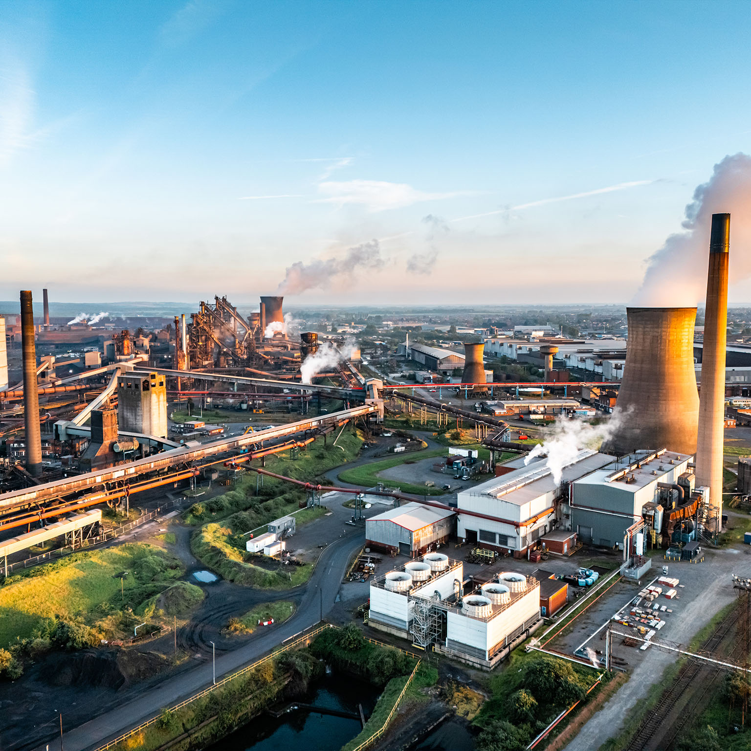 Steel mill emitting smoke and steam at sunset