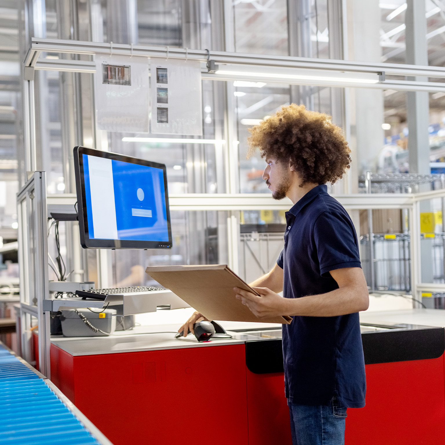 Male worker scanning a delivery package and working on computer at automated warehouse. - stock photo