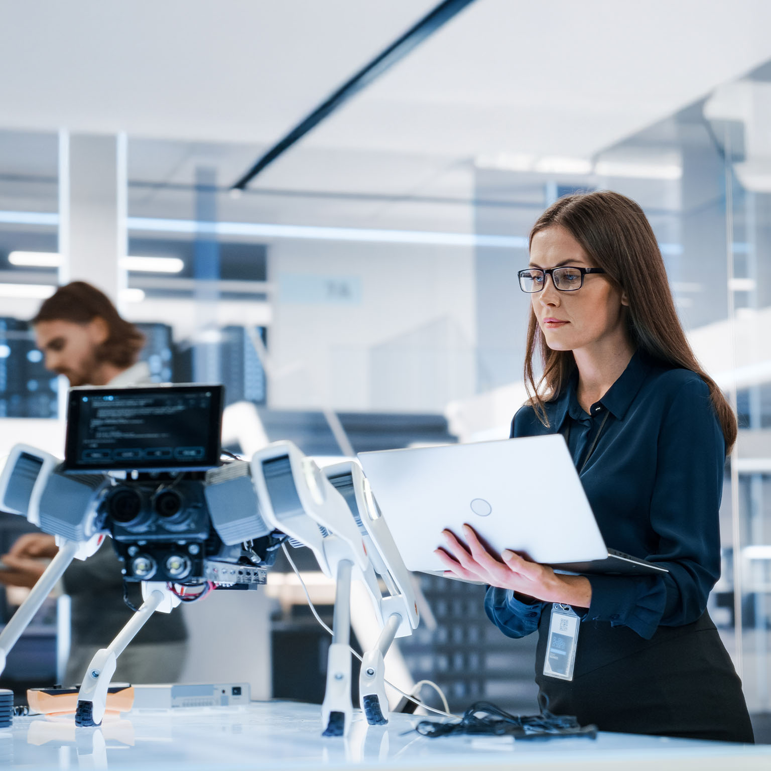 Portrait of a Young Robotics Engineer Using Laptop Computer, Analyzing Robotic Machine Concept in a High Tech Factory.
