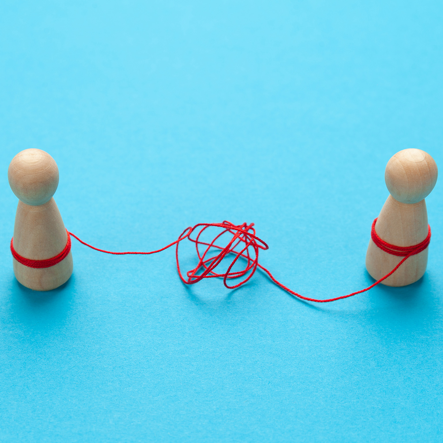 Confused relationships of people in a couple. Two wooden block figures tied together by string tangled in knots.