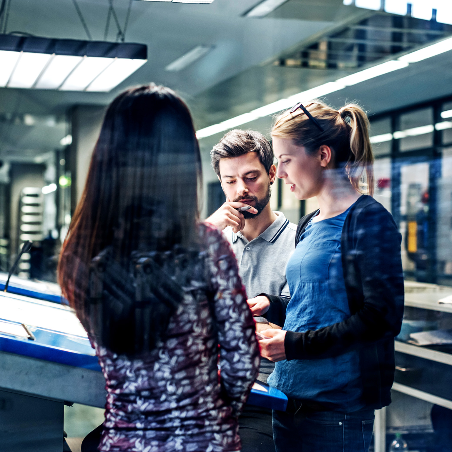 A group of printing plant engineers talking and working together at a large console