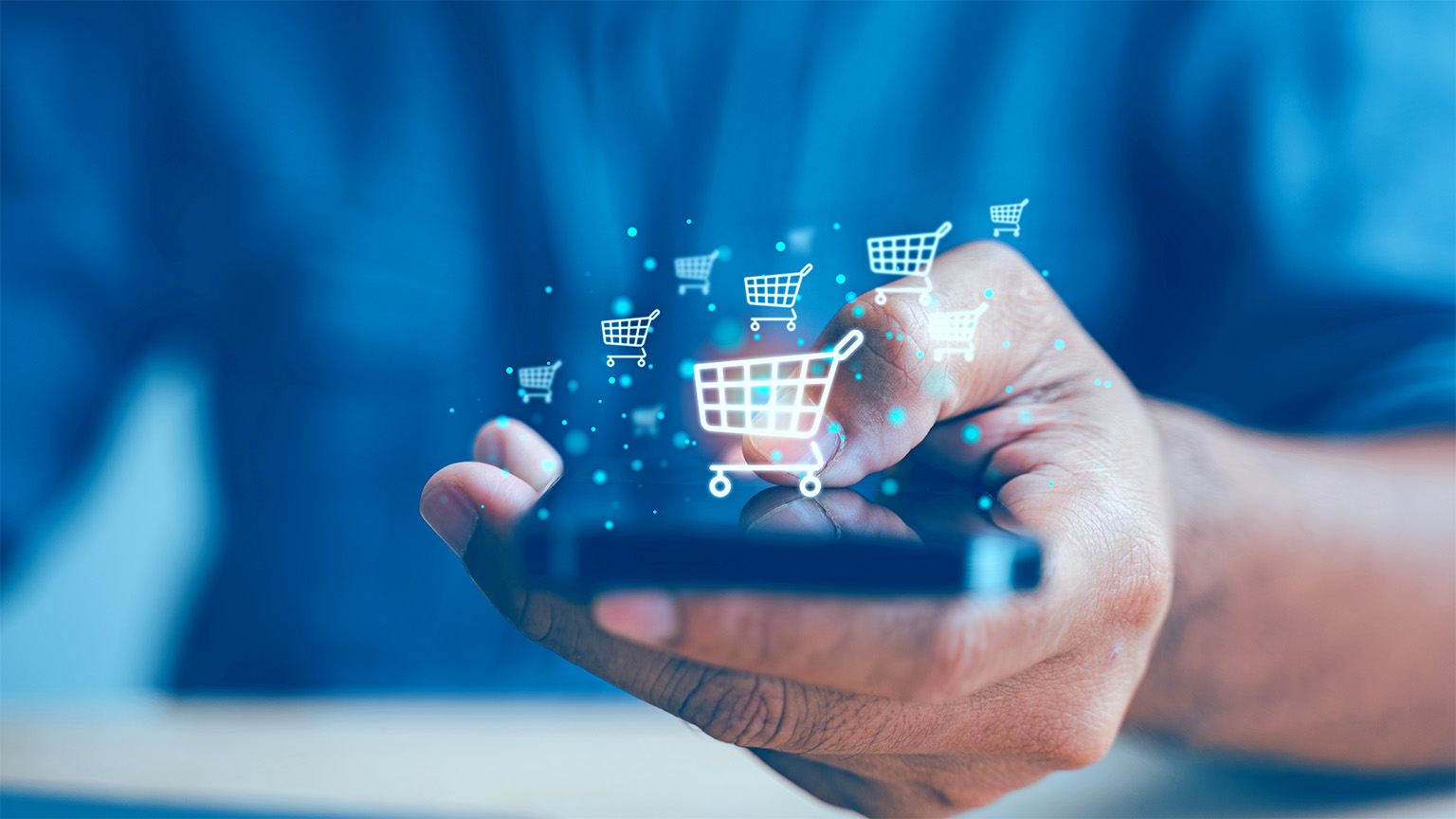 Close up image of a hand holding a smartphone with digital shopping cards floating around it.