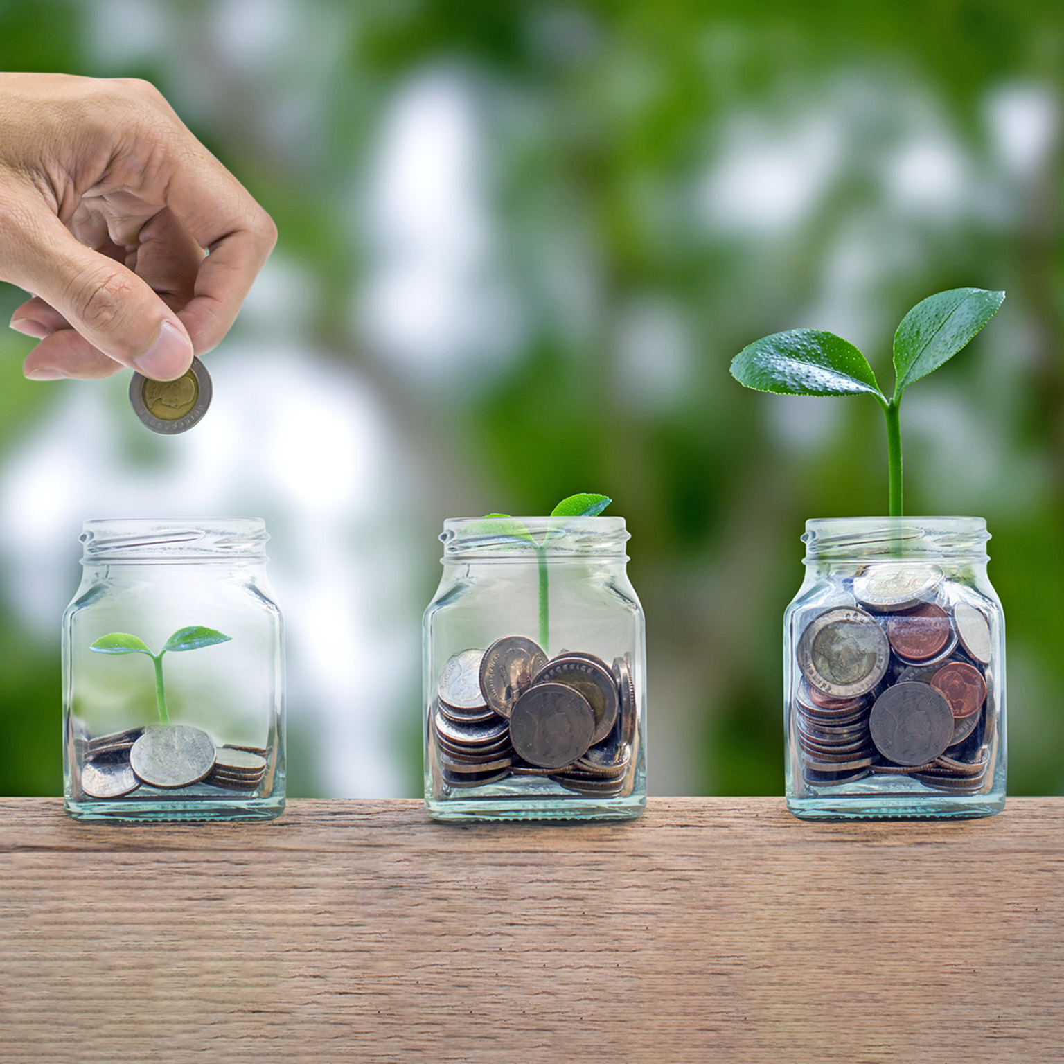 A hand putting a coin into a glass bottle containing coins