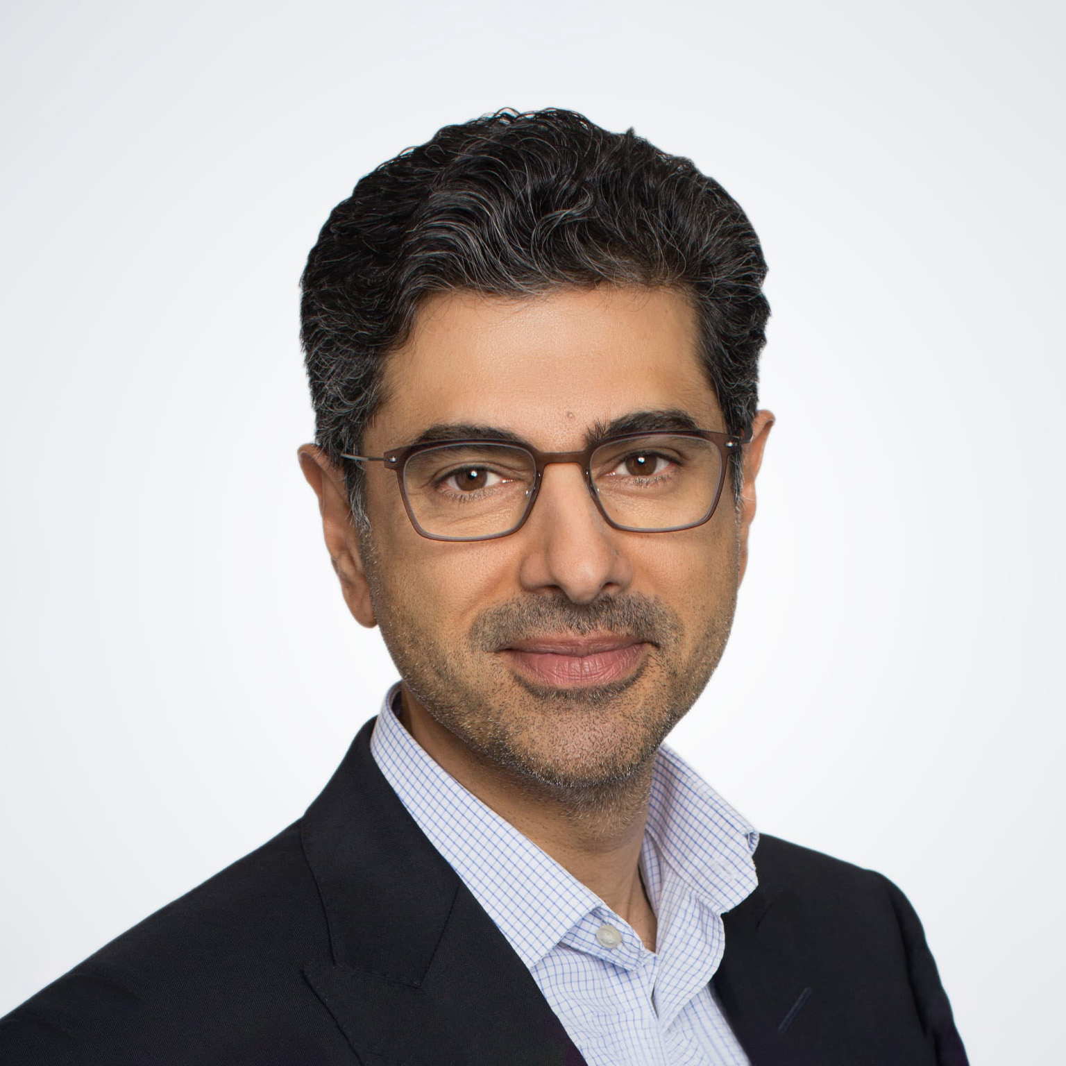 A photograph captures Alok Sama in a suit jacket and button down shirt, smiling gently against a white background.