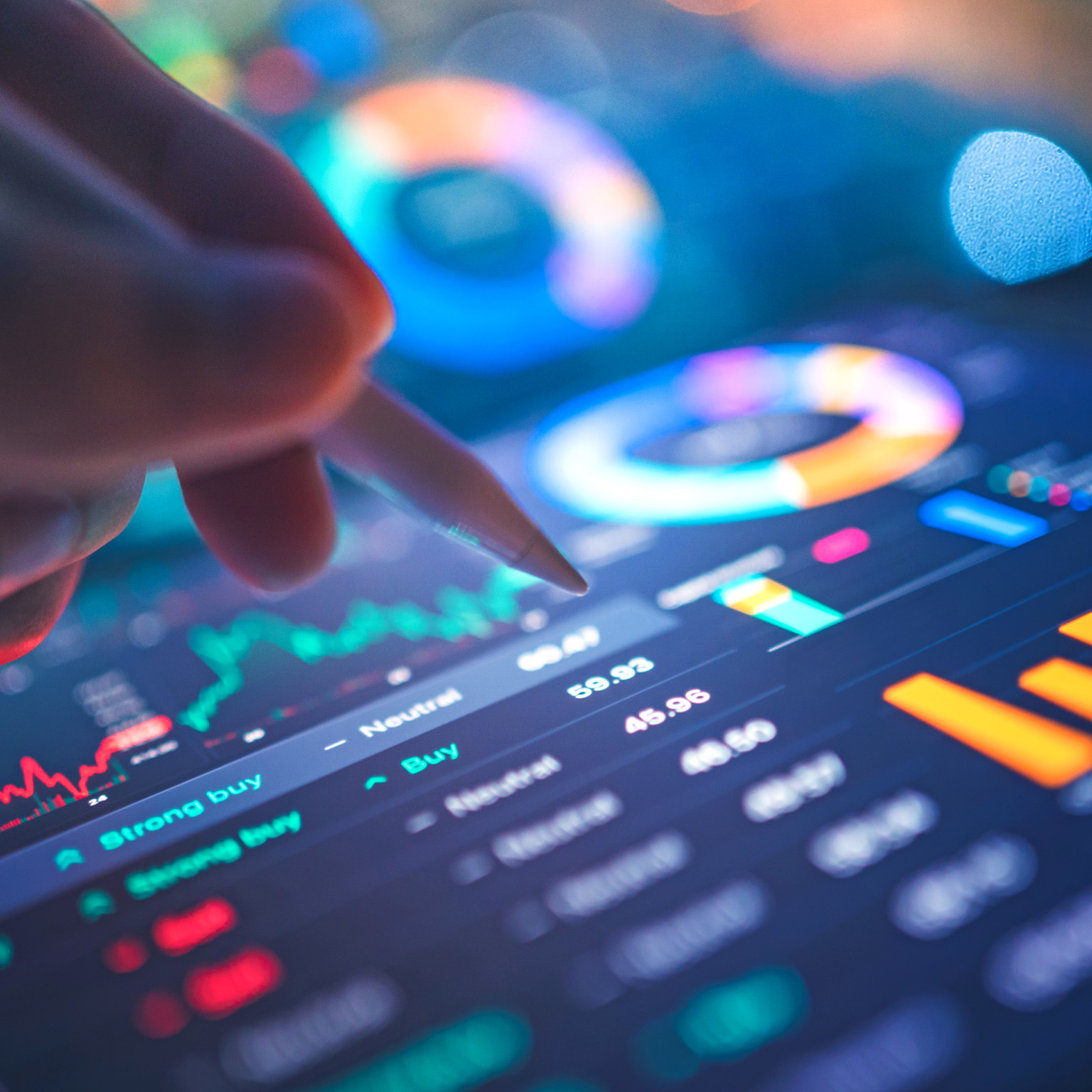 A hand uses a stylus to interact with a tablet displaying financial data and charts, including candlestick charts and pie charts. The screen glows with blue and orange hues.