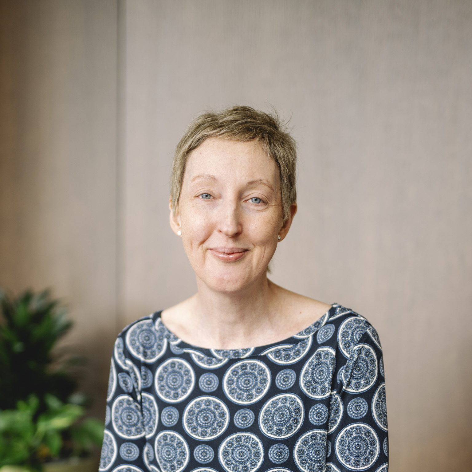 The camera captures CEO Anna Manz's serene smile, framed by her short blonde hair and bright blue eyes. She is wearing a dark blue top with a circular pattern.
