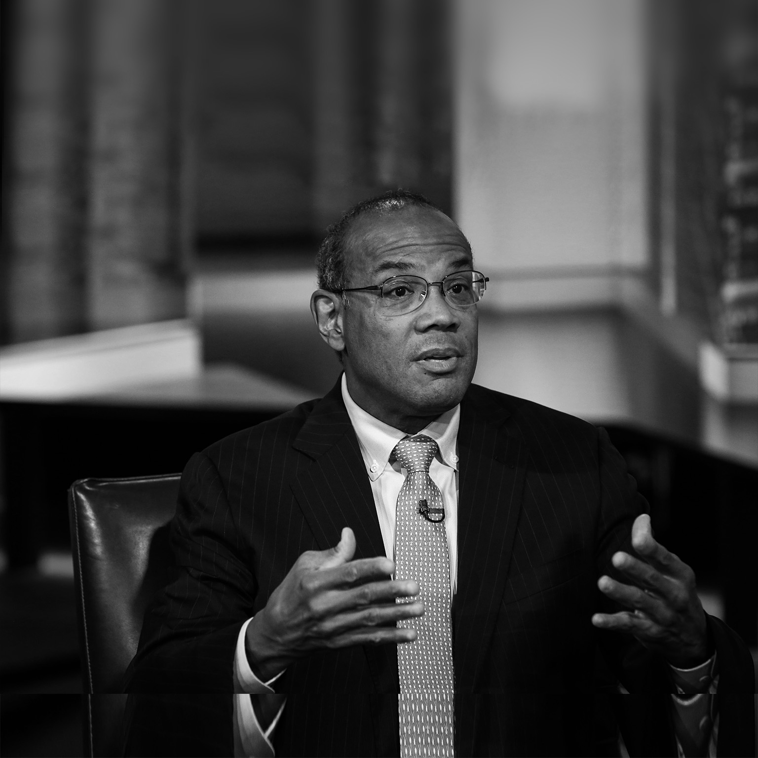 Black and white Portrait of John Rogers in a library appearing to be making a point in a discussion.