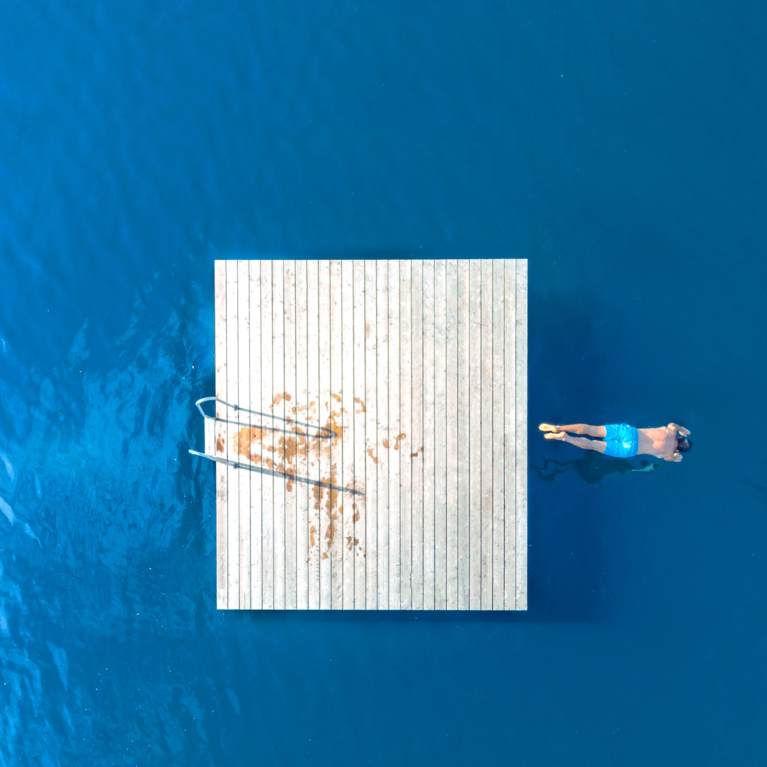Aerial view of a man jumping from a floating dock into a blue lake