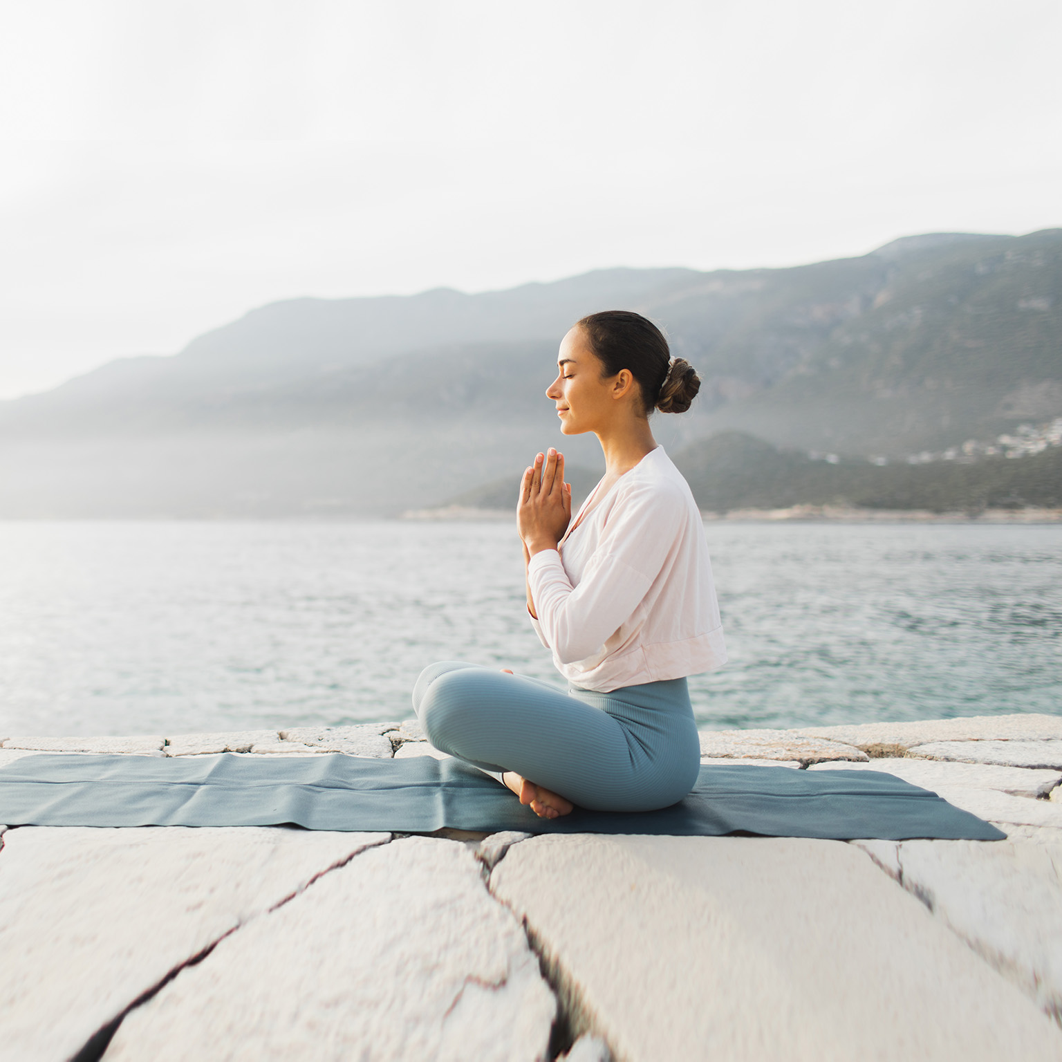 Young woman praying and meditating outdoors by seaside.
