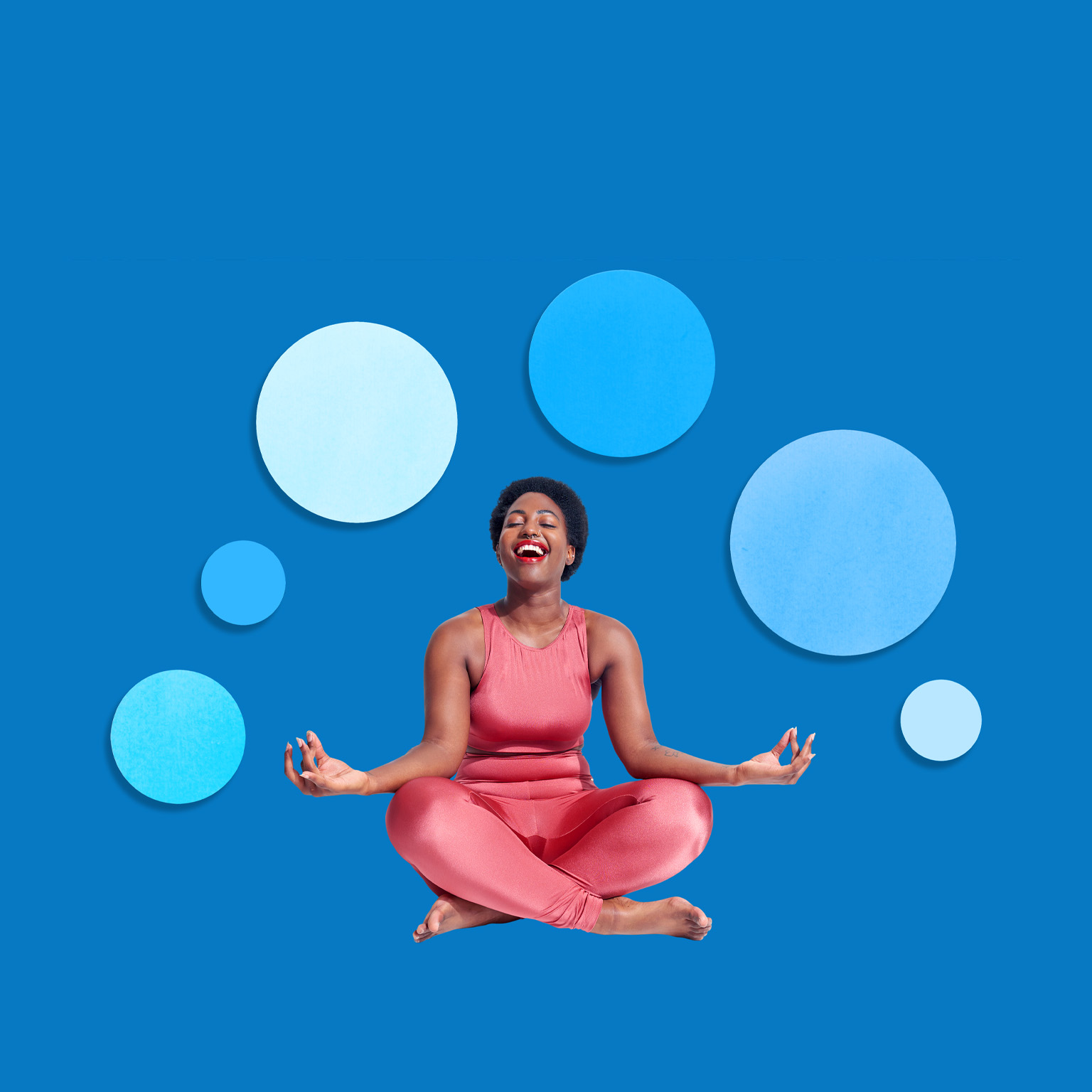 A joyful woman sitting cross-legged in a yoga pose, wearing a bright coral outfit and laughing with her eyes closed. The background is a solid blue with several floating circular shapes in different shades of blue, creating a calm and balanced visual effect.