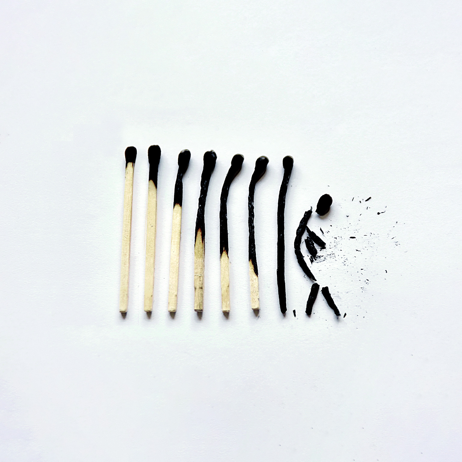 A row of 8 matches that go from lightly to completely burnt. The last match is broken into a shape that resembles a human figure. 