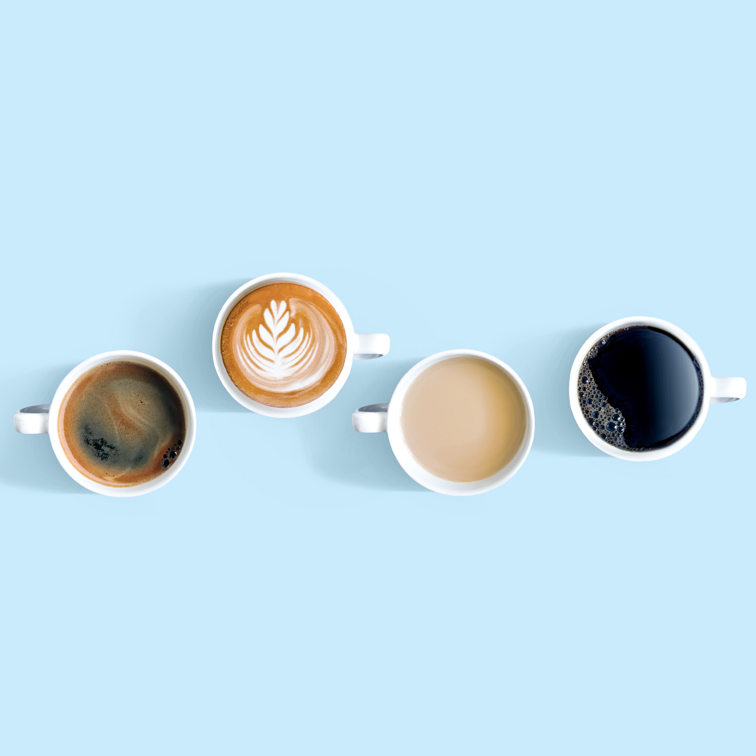 Overhead view of cups with different types of coffee. One of the cups sits higher up in the frame with a foam flourish on top.