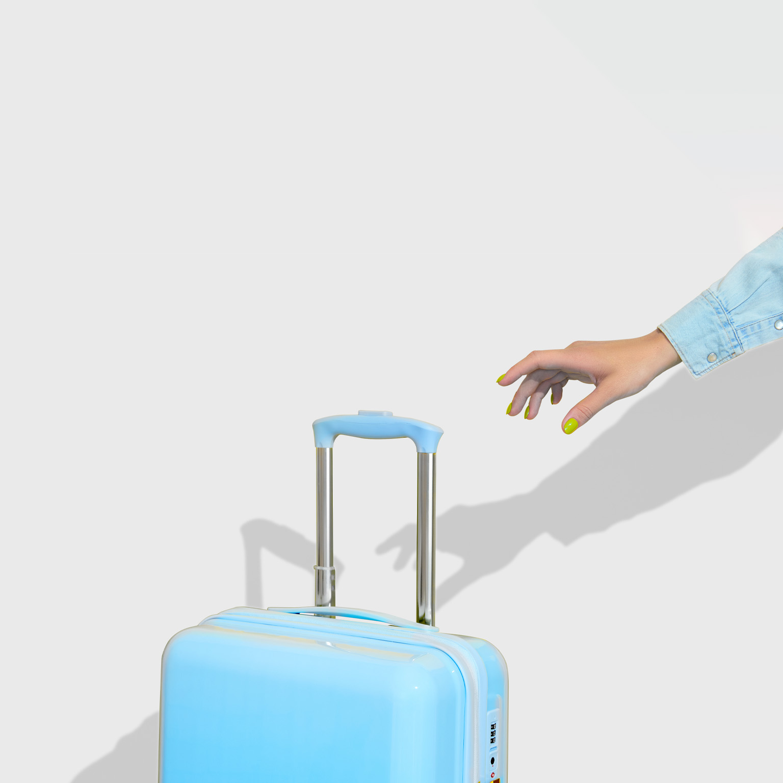 A hand with bright yellow nails reaches for the handle of a blue suitcase.