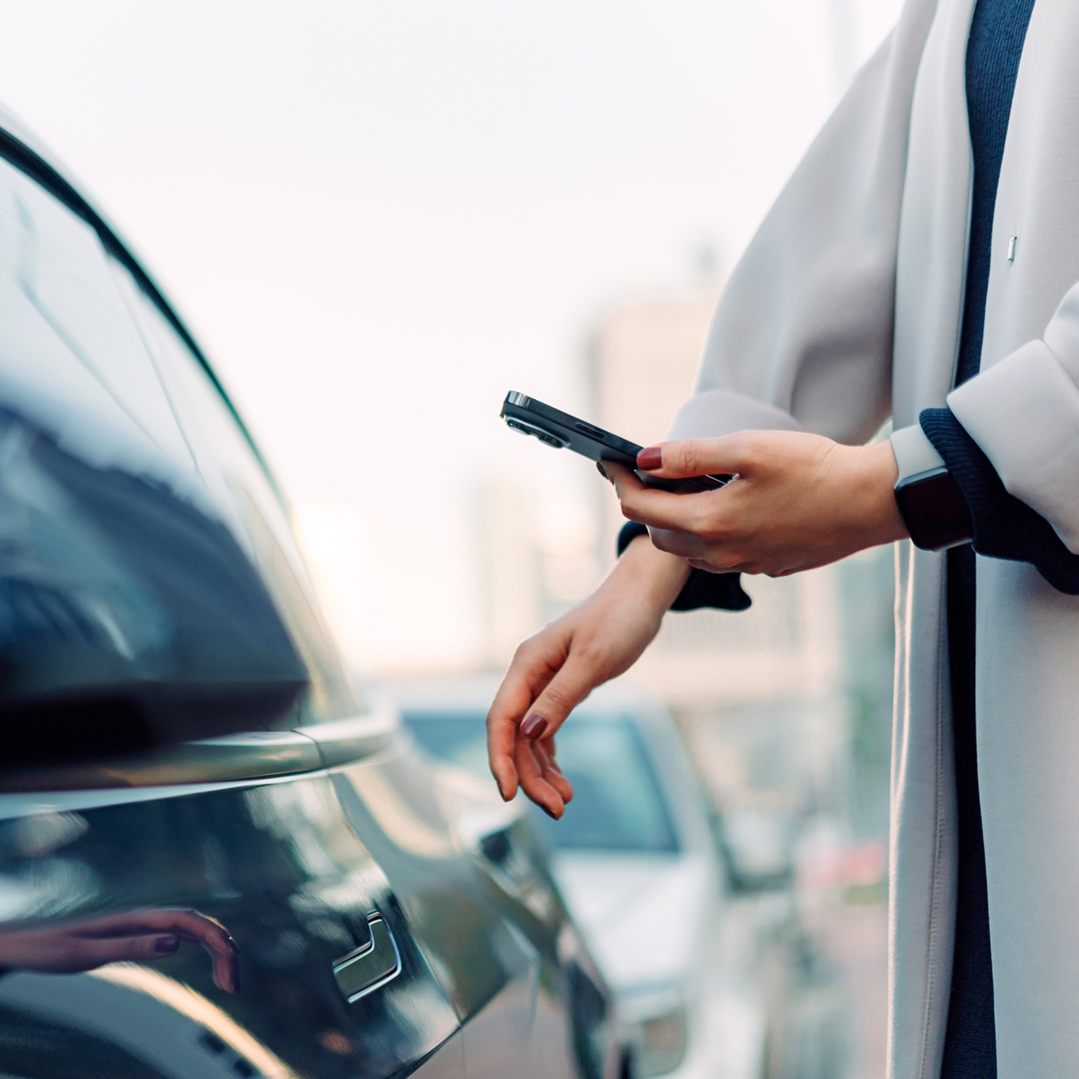 Close up of young Asian woman using mobile app device on smartphone to unlock the doors of her intelligence car in city street