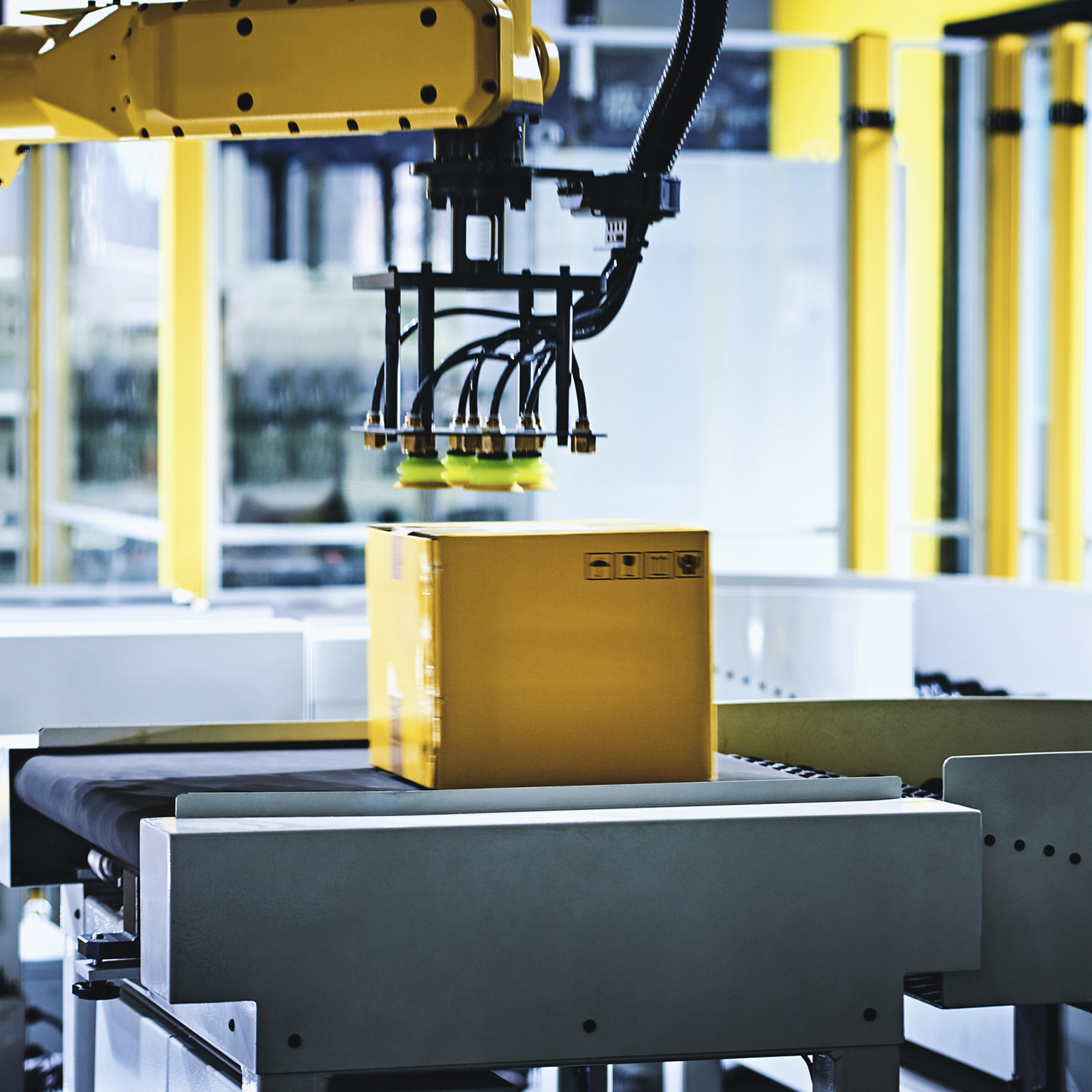 Close-up of robotic arm carrying cardboard box on conveyor belt at modern distribution warehouse.