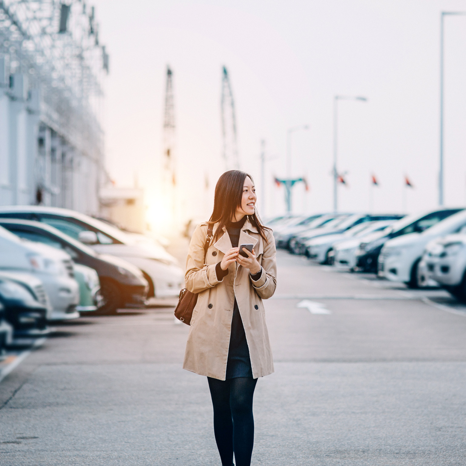 Young lady using smartphone while walking to car in rooftop carpark in city