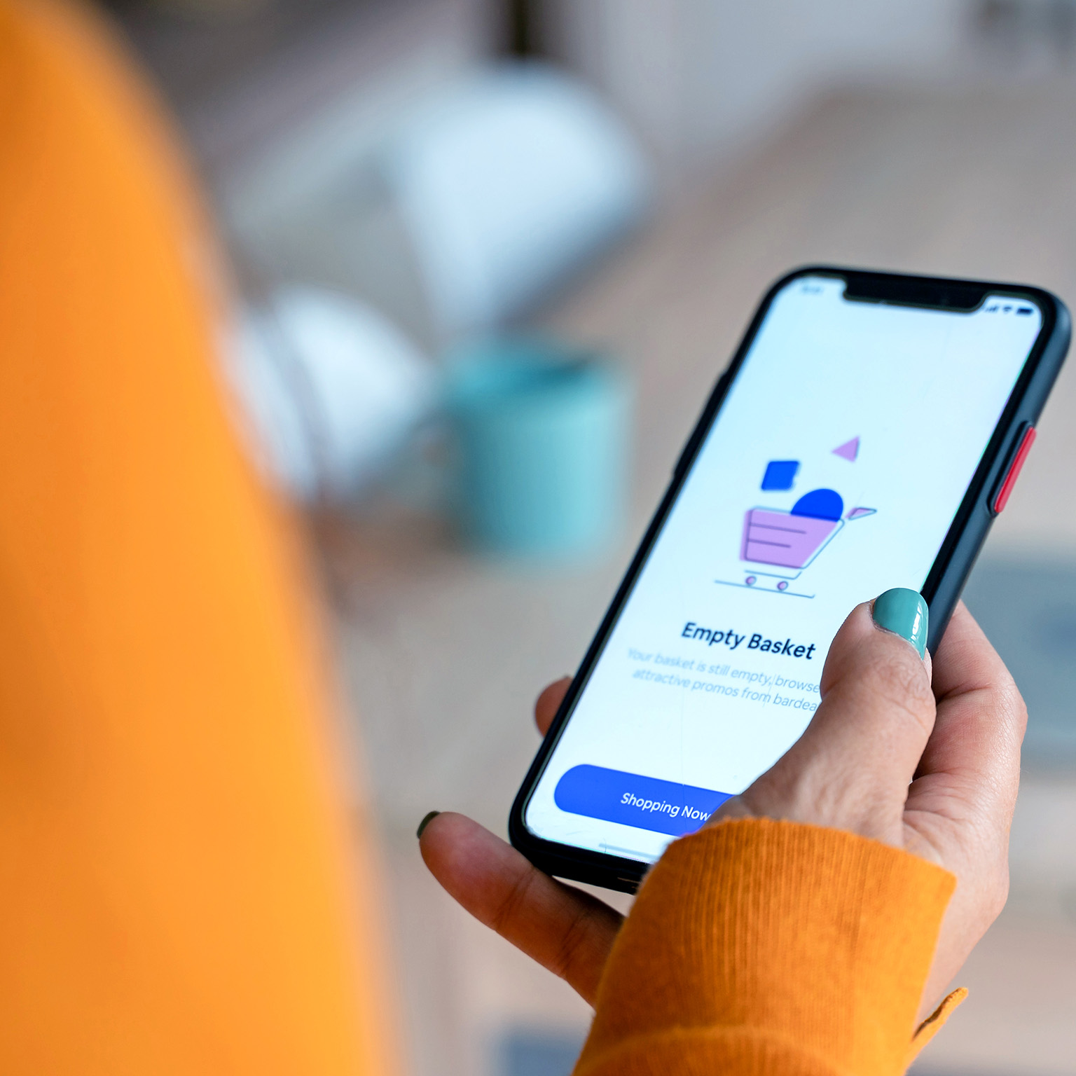 Person in an orange sweater holding a smartphone displaying a shopping app screen that says “Empty Basket” 
