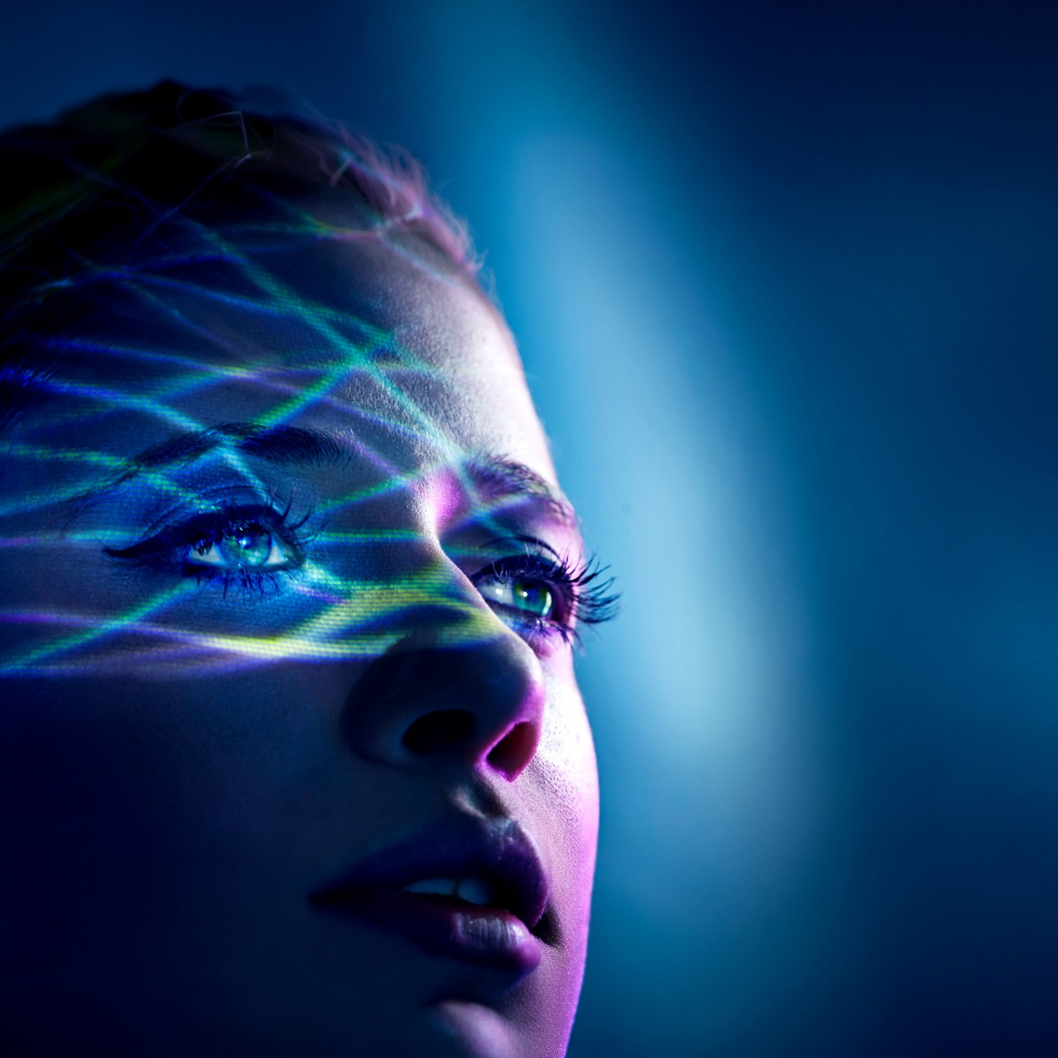 Close-up of a person's face illuminated by colorful digital light patterns, looking upward.