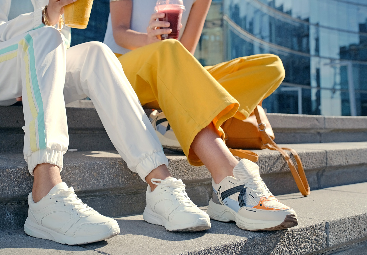 Close up image of two friends sitting on a set of stairs with their legs and shoes in the foreground.