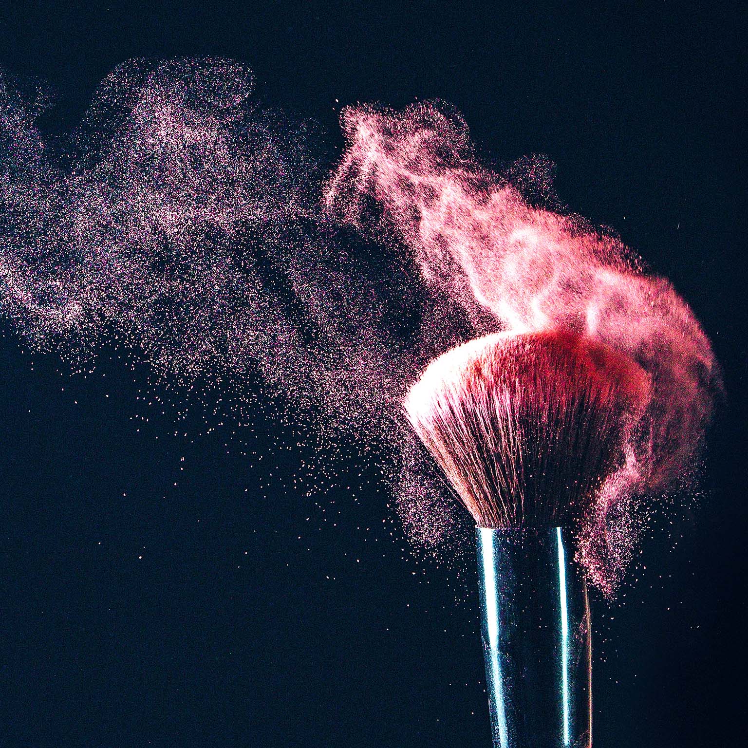A makeup brush with blush particles artistically being shaken off