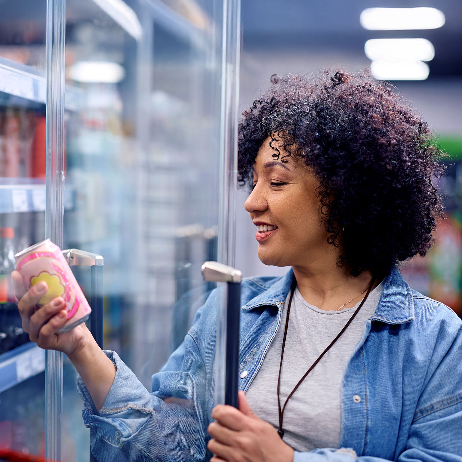 Happy woman holding a can of soda at refrigerated section in a supermarket