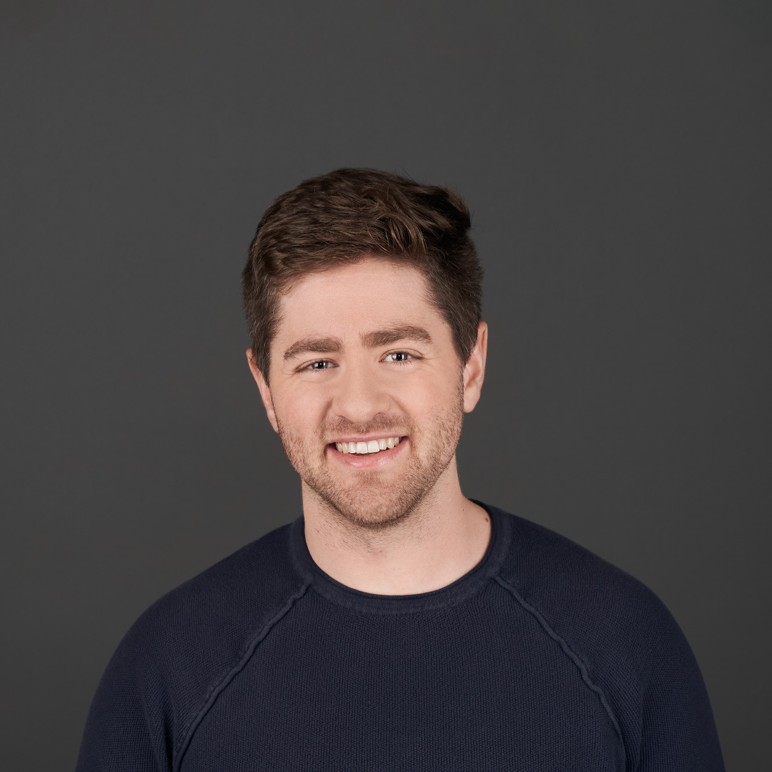 Eric Glyman with short brown hair and a trimmed beard smiling during an interview. He is wearing a dark jacket over a light-colored shirt, with a softly blurred indoor background behind him.