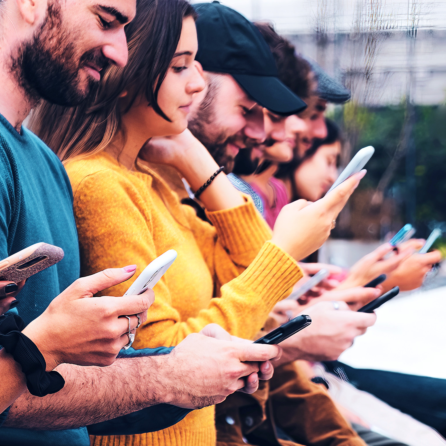 Closeup image of a group of interracial gen-z friends sitting outdoors in a row, looking at and interacting with mobile phones.