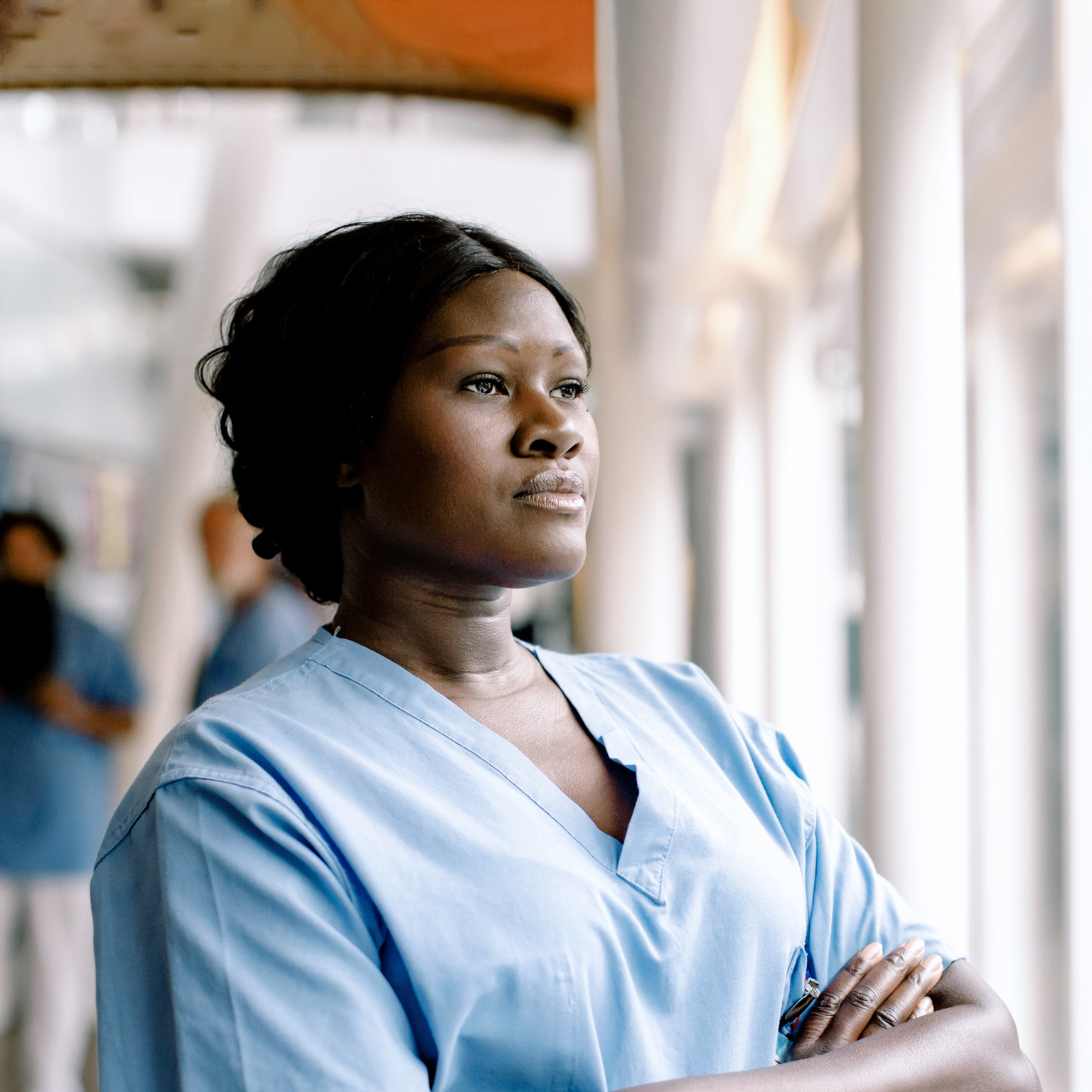 Contemplating female nurse with arms crossed looking through window in hospital