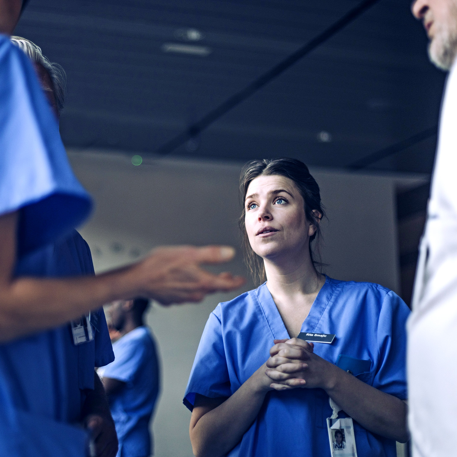 An attentive nurse, whose face shows a look of thoughtful consideration and slight apprehension, having a discussion with another nurse in a hospital hallway.