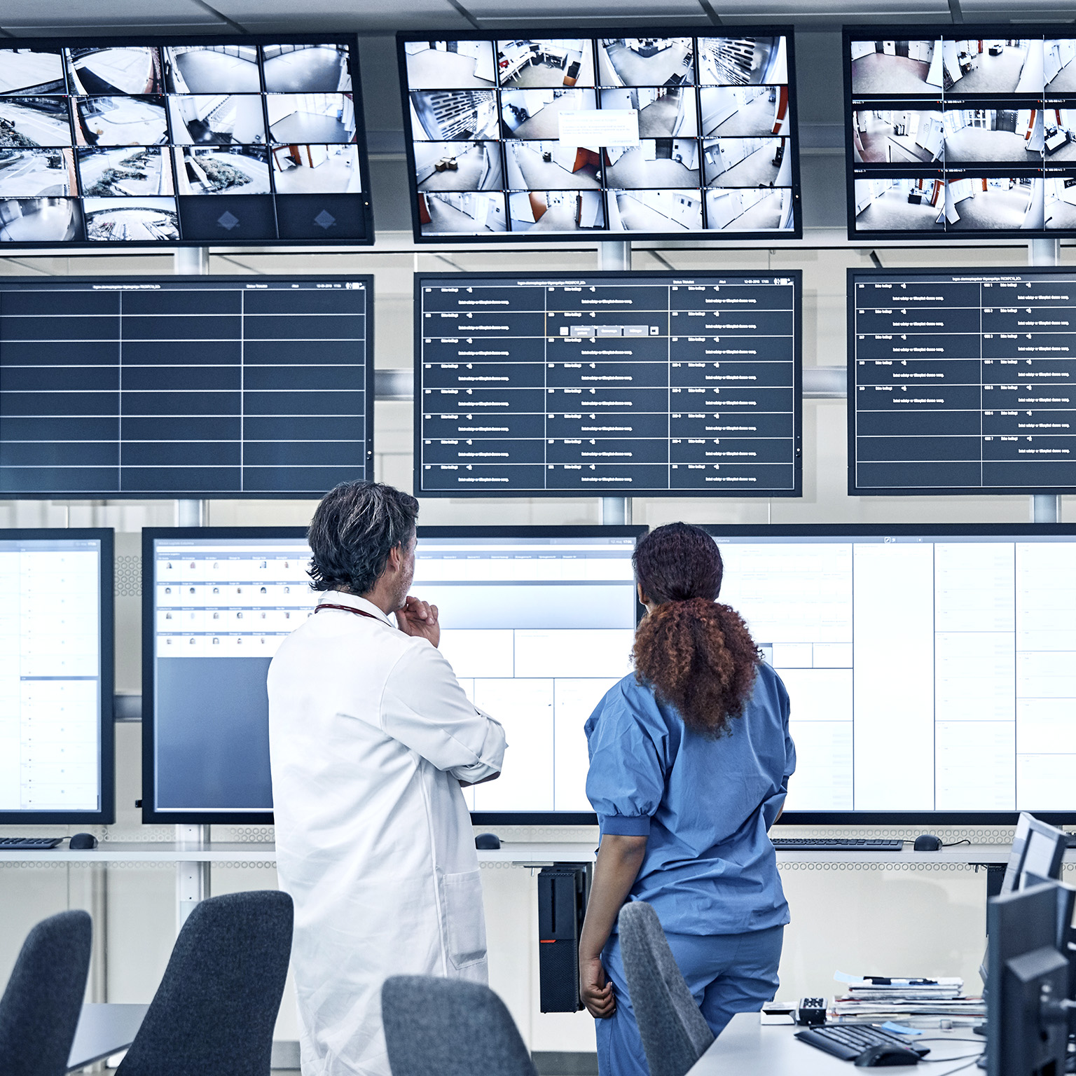 Medical professionals discussing the security system in front of an array of screens in a control room.