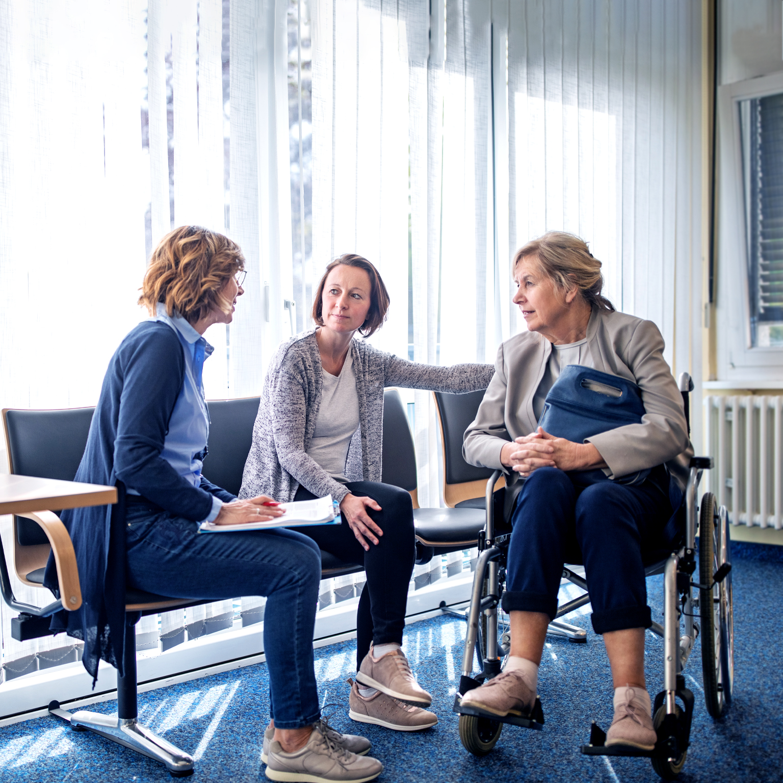 A social worker talking to an elderly woman in a wheelchair and her daughter in a hospital setting.