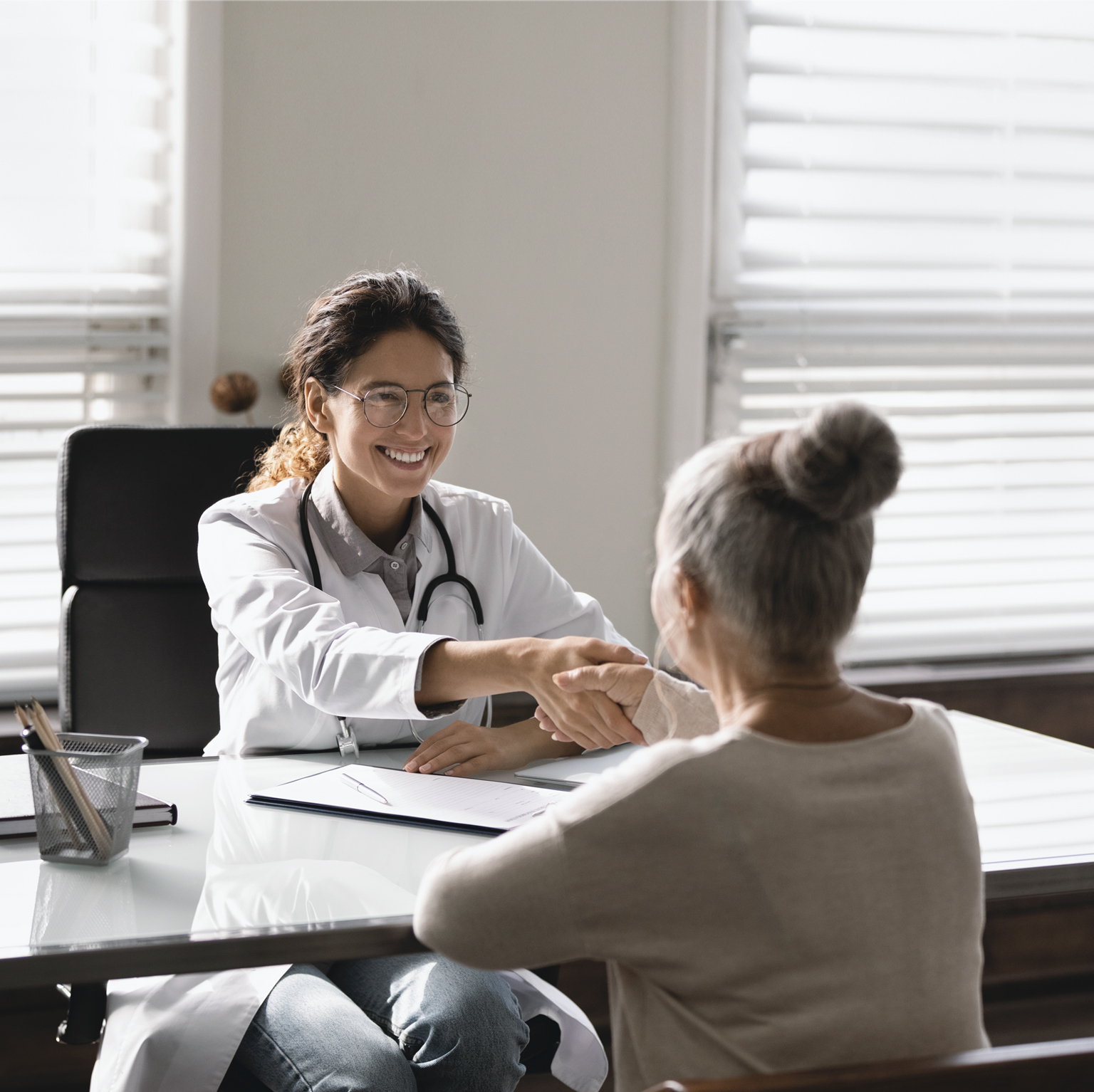 Young Hispanic female doctor shaking hand of senior woman patient