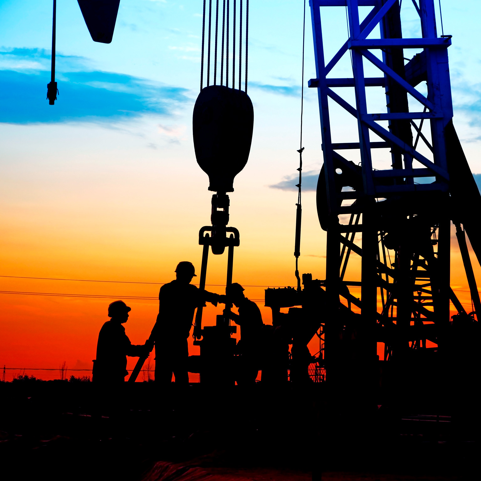 Silhouetted workers operating an oil drilling rig, against a vivid sunset sky with gradients of orange, red, and blue.