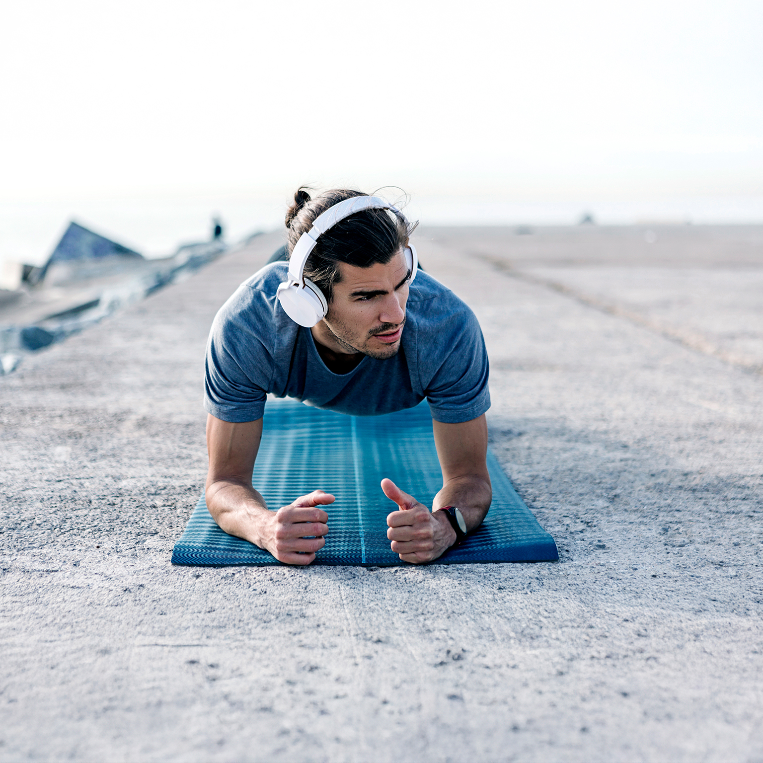 Young man wearing headphones planks on blue yoga mat