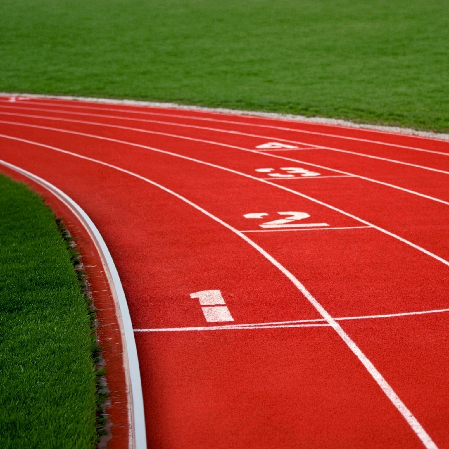An empty red running track curves through a green field, with white lane markings and the numbers one through four visible, suggesting competition, positioning, or the importance of starting point.