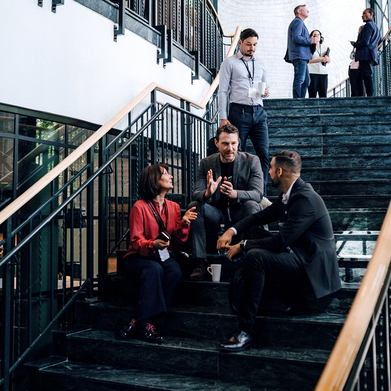 Two men and a woman sitting on the staircase landing engaged in a discussion