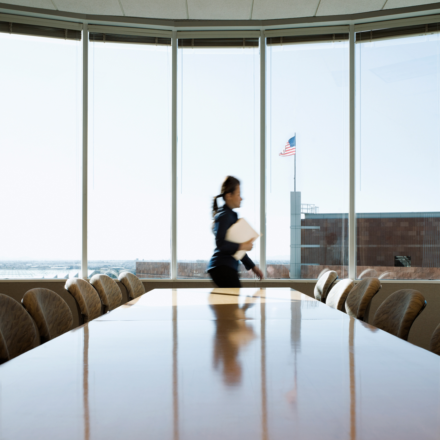 Hispanic businesswoman rushing through conference room, an American flag is seen though the window on top of an adjacent building