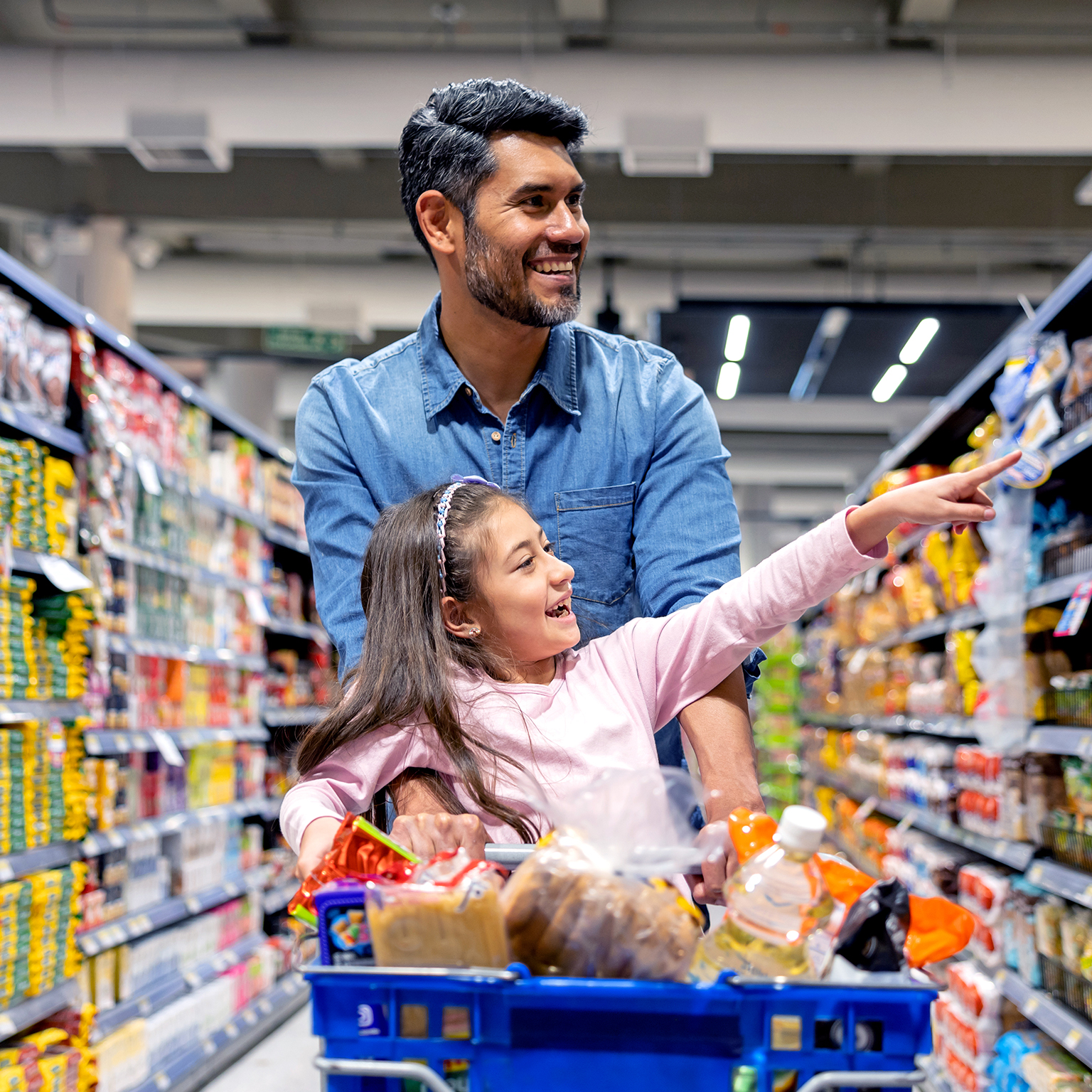 Happy Latin American girl shopping with her father at the supermarket and pointing away at a shelf
