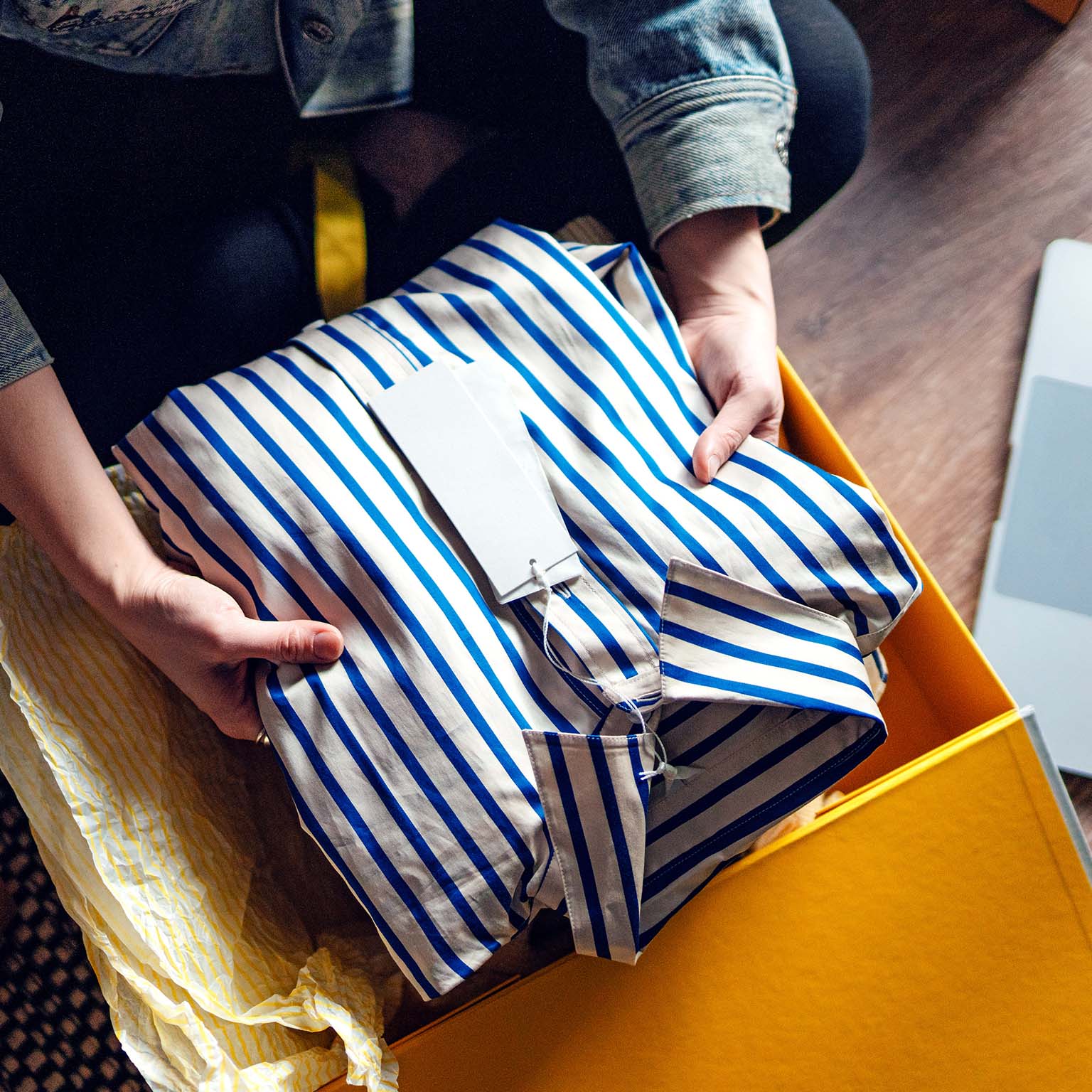 Elevated view of young woman unboxing a delivery from home shopping, with a laptop by her side.