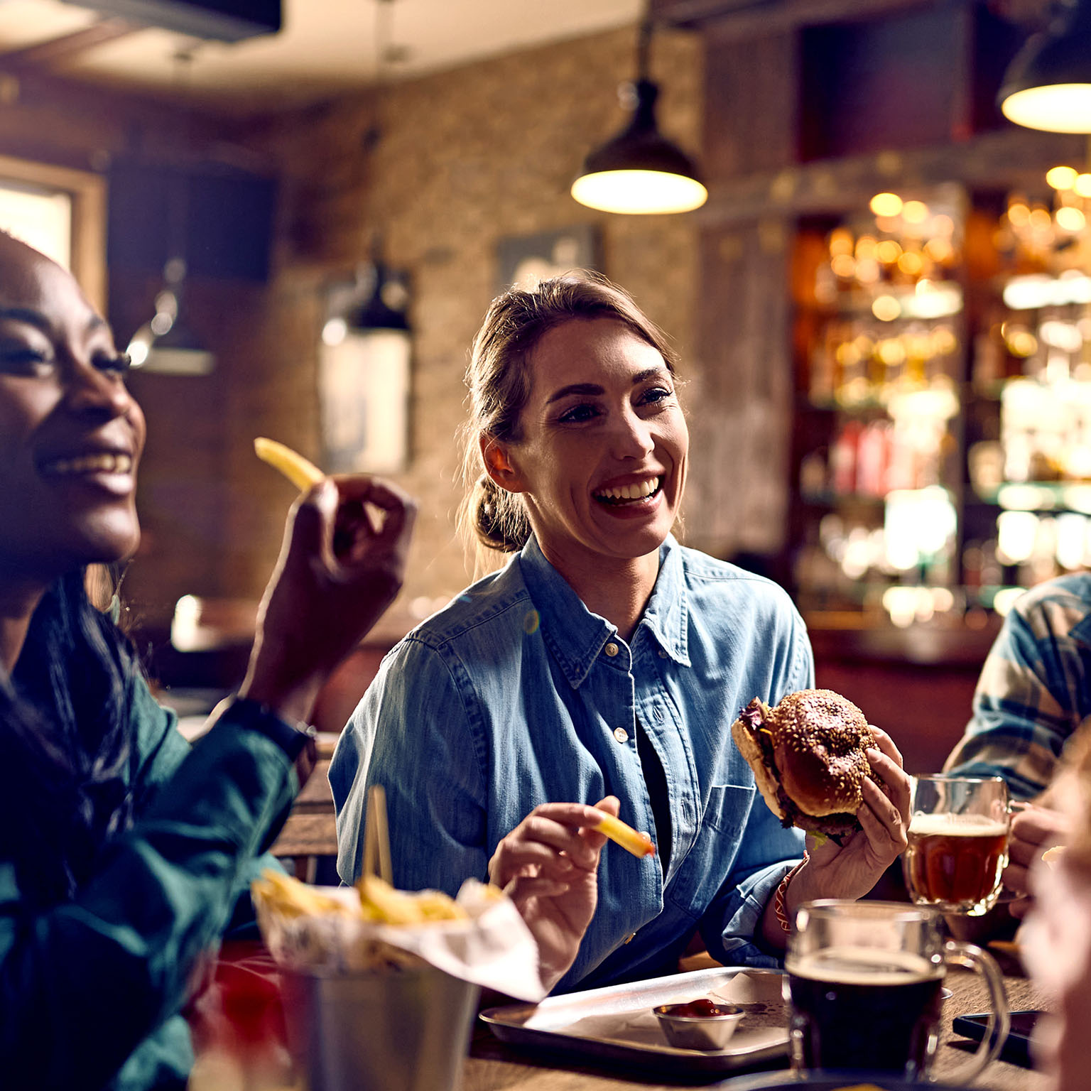 Multiracial group of happy friends eating burgers while drinking beer in a pub.