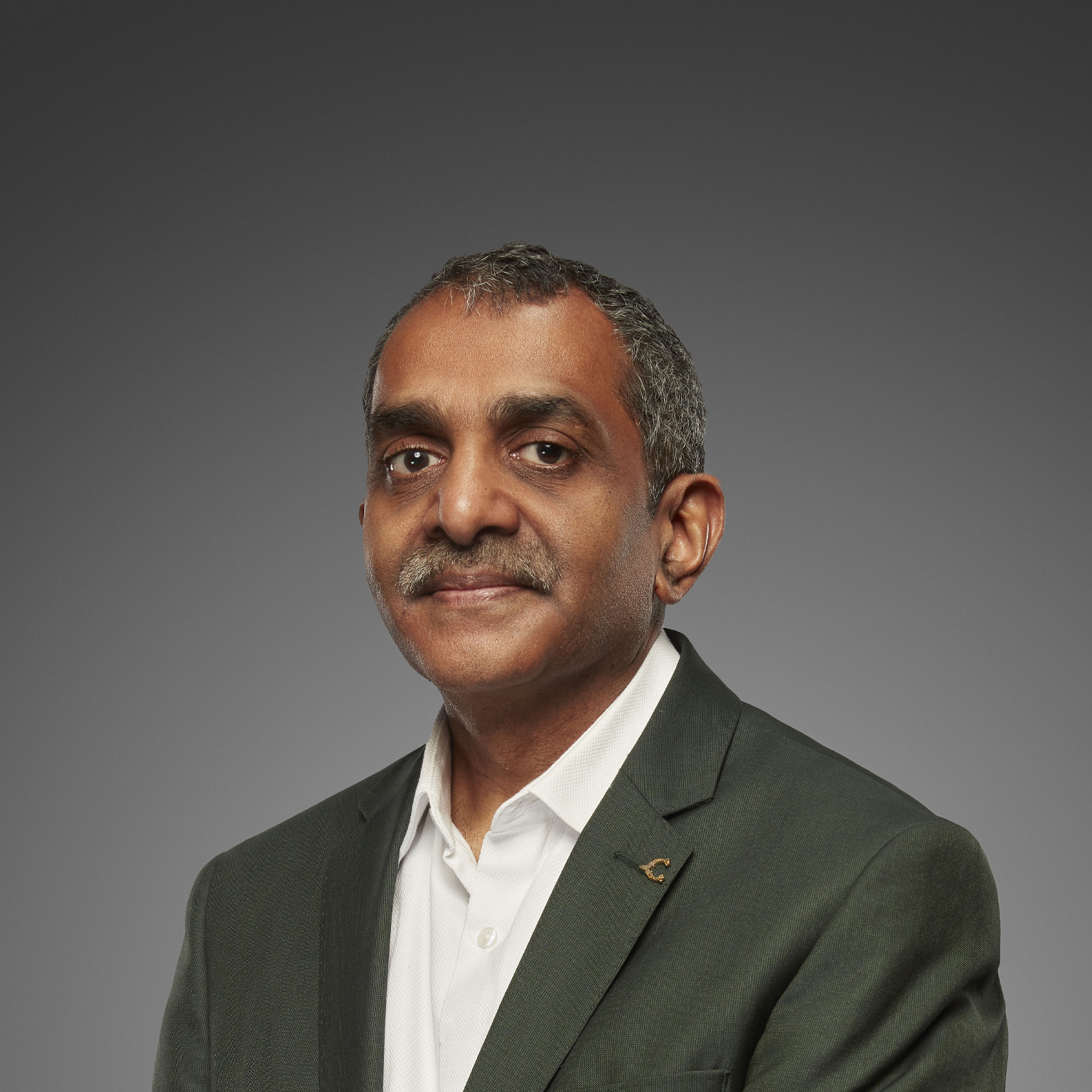 A portrait of Vijay Anand Guntur shows him wearing a gray suit jacket and a white button down shirt, exuding confidence with his gaze. He has well-groomed salt-and-pepper hair and a mustache.