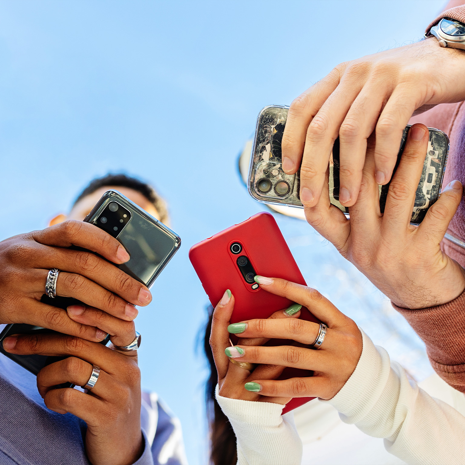 Low angle view of three young people using mobile phones outdoors - stock photo